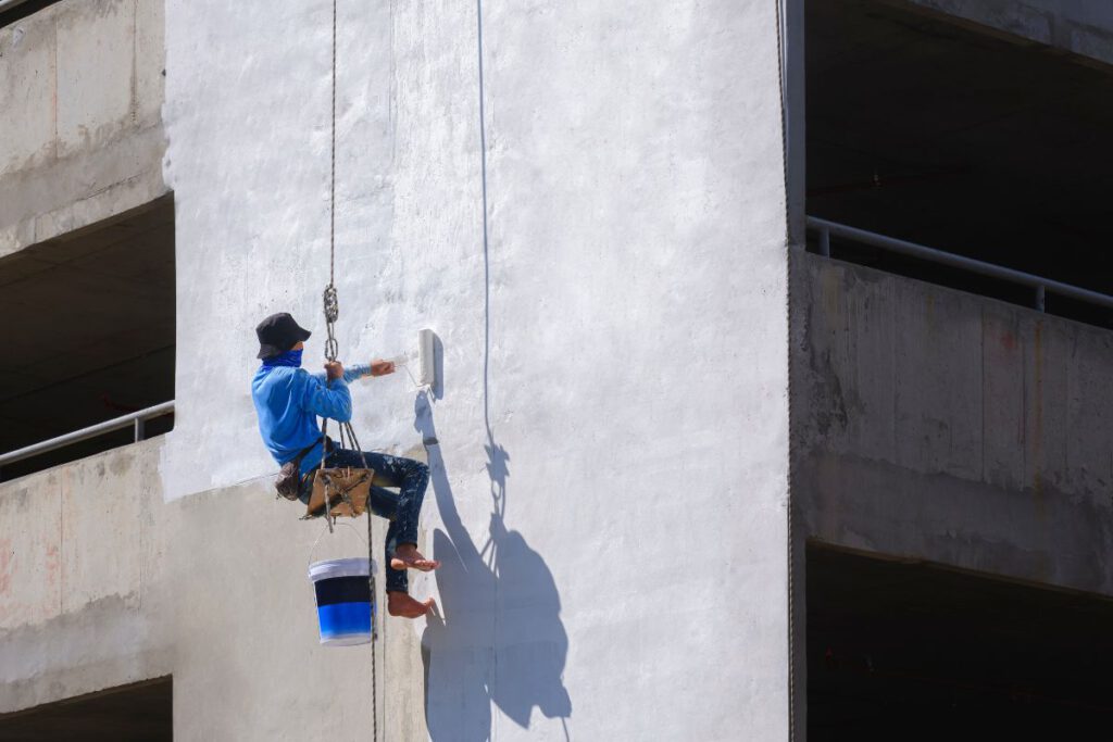 worker rappelling to painting white primer on exterior wall of parking garage building in construction site